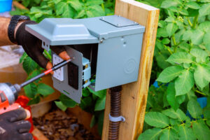 A technician installing a new outlet next to a garden.